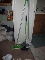 Swiffer mop, broom, and dustpan standing upright on carpet near bathroom area
