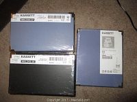 Five IKEA Kassett storage boxes with lids in original packaging, two blue and three black boxes.