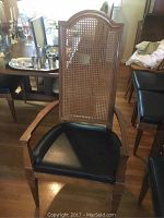 Captain chair with high arched woven cane back, wooden frame and black cushioned seat with armrests, showing light wear.