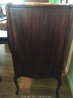 Front view of wooden music cabinet showing single door and bowed legs.