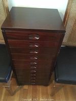 Front view of tall dark wood music cabinet with 11 recessed handle drawers.