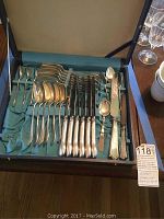 Full view of flatware set arranged in a case with blue satin lining, showing spoons, forks, knives, one small spoon, and other utensils