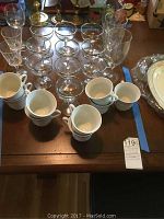 Top view of all the glassware including 10 clear glasses, 9 stacked white coffee cups, and multiple wine glasses grouped on a table.