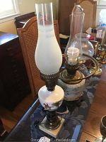 Front and side view of three oil lamps on a table showing details of chimneys, painted bases, and overall condition.