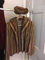 Full view of the vintage tan fur coat hanging on a rack with matching fur hat above it.