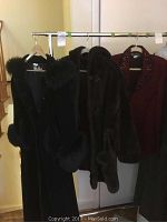 Three coats hanging on a rack: black fur-accented coat, brown coat, red coat with bead embellishments visible.