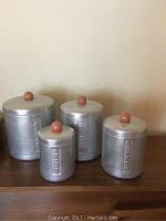 Set of four vintage metal canisters labeled flour, coffee, sugar, and tea, arranged in size order from largest to smallest on a wooden surface.