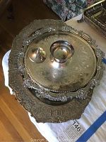 Five silver plated items including three platters with elaborate engraved patterns and scalloped edges, and one small bowl. Items show tarnish and age wear.