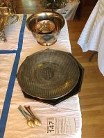 Photo of round silver serving bowl, two plates (one octagonal, one round with emblem), and three small silver spoons with colored handles on white cloth.