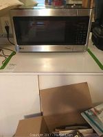 Front view of LG microwave oven sitting on a countertop. Shows full unit with silver body and black glass door with keypad.