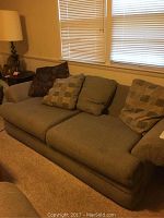 Full view of the upholstered sofa against a wall with window blinds, showing cushions and armrests