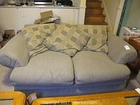 Front view of light gray upholstered loveseat with four swirl-patterned cushions, showing overall shape and style, some wear visible on cushions and seat.