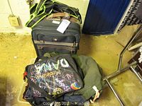 Photo of black rolling suitcase with brown handle and blue hard-shell suitcase in background on floor.