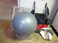 Exercise ball and tennis rackets stacked on storage bin with baby gate and foldable cart in background