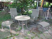 Outdoor setting with round stone top table and two metal framed cloth chairs with two matching footstools. The chairs and footstools show holes and tears in the fabric.