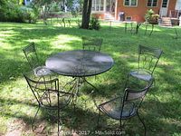 Overview of round wrought iron patio table and four matching chairs on grass outdoors