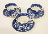 Three Blue Willow cups and matching saucers arranged on a white surface showing the classic blue and white pattern.