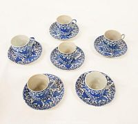 Six blue and white porcelain espresso cups and matching saucers arranged on a white surface, showing the chintz style floral and bird pattern.