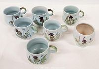 Photo of six stoneware cups with hand-painted thistle and wildflower motifs, pale blue exterior with loop handles.