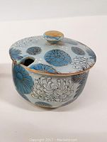 Mustard pot with lid on, showing blue and gray chrysanthemum floral pattern and gold trim accents on knob and rim.