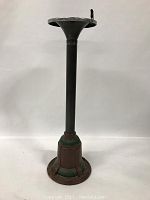 Vertical view of the pendant light fixture base showing the mounting plate, cylindrical post, and wider decorative base with painted brown and green surfaces.