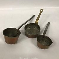 Three small copper pots arranged in a line showing front and side views, highlighting the different handle styles and pot shapes.