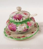 Front view of the floral mustard pot with under plate and spoon, showing pink floral pattern and green scalloped edges.