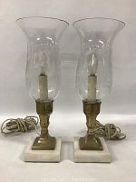 Pair of brass and marble table lamps with clear glass hurricane shades and electrical cords.
