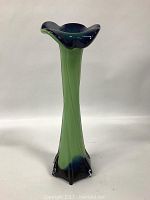 Full view of tall green blown cased glass vase with dark blue at base and rim