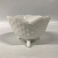 Front view of the white milk glass hobnail bowl showing its rounded hobnail pattern, scalloped rim, and one of three small feet supporting it.