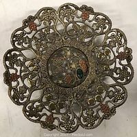 Full view of filigree brass decorative plate, showing ornate grapevine design and central colored emblem