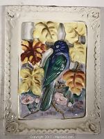 Ceramic bird wall plaque with a blue and green bird surrounded by raised yellow and brown leaves, pink flowers, and a decorative white rectangular frame with floral impressions at corners.