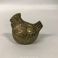 Side view of small brass chicken figurine showing textured surface and rounded shape.
