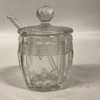 Clear crystal mustard container showing cut glass design on sides, faceted knob lid, and clear glass spoon inside.