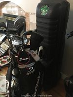 Front view showing TaylorMade stand bag with various club headcovers and a black hard plastic travel case in background