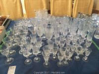 Wide view of the collection of assorted crystal glassware laid out on a table showing multiple rows of different glass types.
