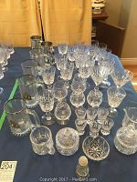 Wide view of table showing assortment of crystal and glass barware including beer steins, snifters, wine glasses, cream, sugar, and smaller glass items