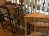 Photo showing two metal wine racks and one wooden corner side table with drawer and shelf, placed near stair railing.