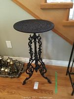 Full view of ornate cast iron side table showing overall structure and height next to stairs.