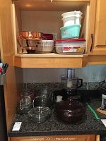 Photo of various glass bowls, food storage containers, and a copper metal warming tray on kitchen countertop and shelf.