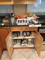 Photo of kitchen drawer and open cabinet packed with kitchen utensils, cutlery trays, and small appliances.