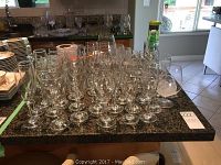 Full view of the bar glassware collection arranged on a granite countertop including multiple glasses and some other kitchenware in the background
