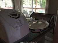 White Black and Decker All-in-One bread maker on a kitchen counter with bread box and glass dishes in background.