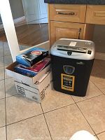 Full view of Fellowes paper shredder next to open box containing Philips Speech Mike items and box of copy paper on tiled floor, wood cabinetry background.