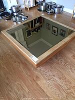 Top view of square coffee table showing oak frame and large mirrored glass top reflecting ceiling and pictures.