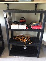 Full view of black 4-tier shelving unit with items displayed on shelves including cables, headset boxes, and power strip.