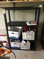 Black plastic 4-tier shelving unit with boxes on lower shelves and empty top shelves.