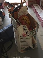 Electric hedge trimmer handles and multiple orange and yellow extension cords coiled in a worn cardboard box.