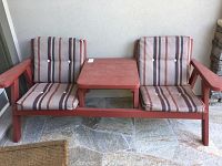 Front view of the red painted wood 2-seater bench with center table and striped cushions.