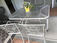 Overview of metal patio table with tempered glass top and two metal chairs, showing decorative scrollwork and outdoor setting.